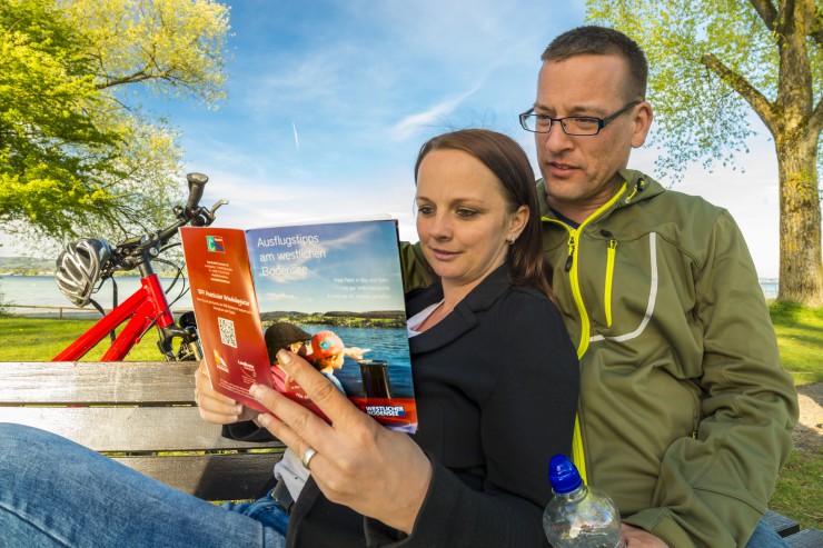 Ein Paar, das Pause auf einer Bank macht und sich ein Reisemagazin anschaut