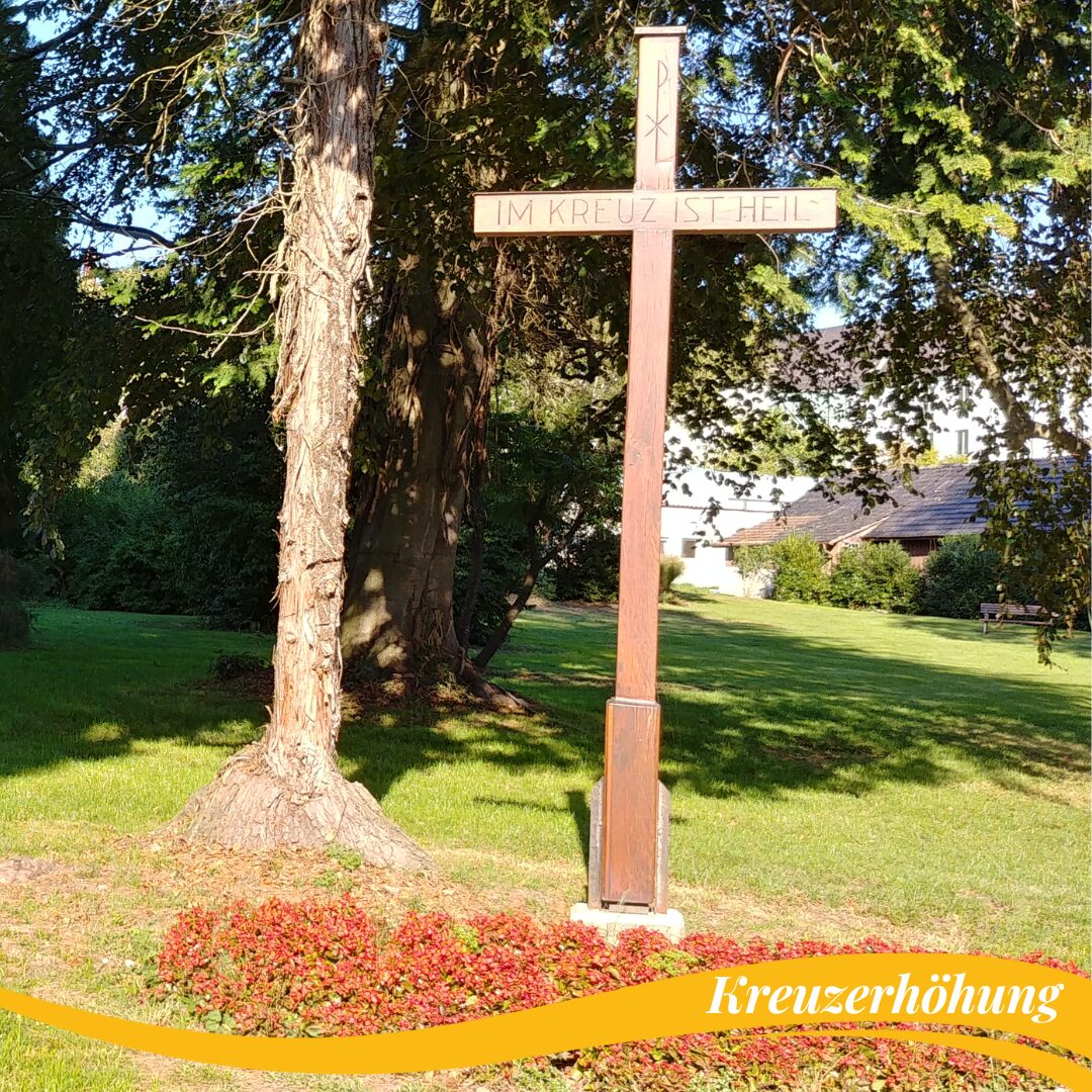 ein Holzkreuz unter einem Baum mit roten Blumen davor